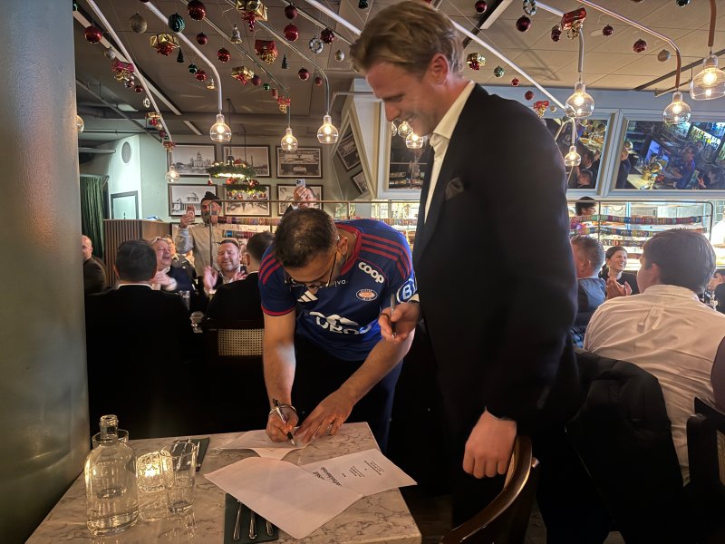 Daglig leder Baljit Singh og Andreas Aalbu signerer avtalen for det neste året foran 100 andre partnere (Foto: Vålerenga)
